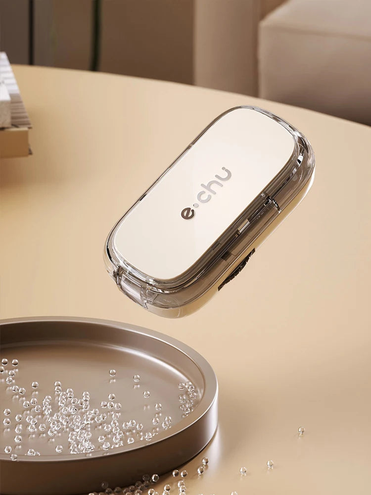 Beige Adjustable Pill Cutter by e.chu, closed and floating above a tray of scattered pills, showcasing its sleek design.