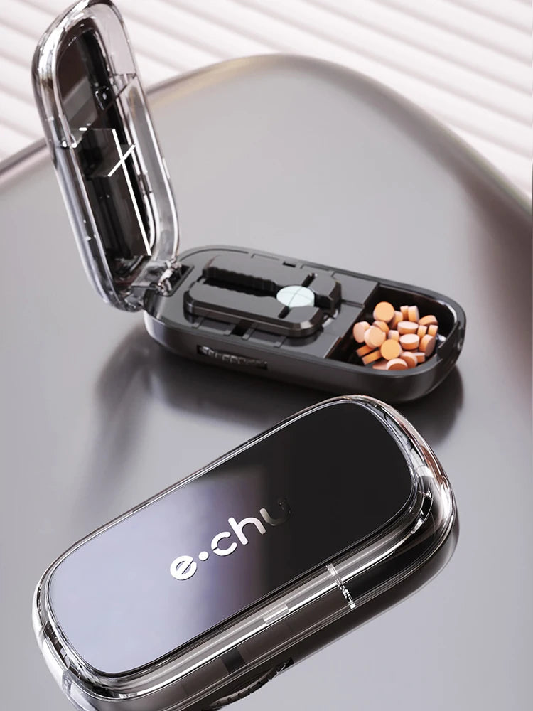 Beige and gray Adjustable Pill Cutters by e.chu, one open with pills and one closed, on a round beige surface with blinds in the background.