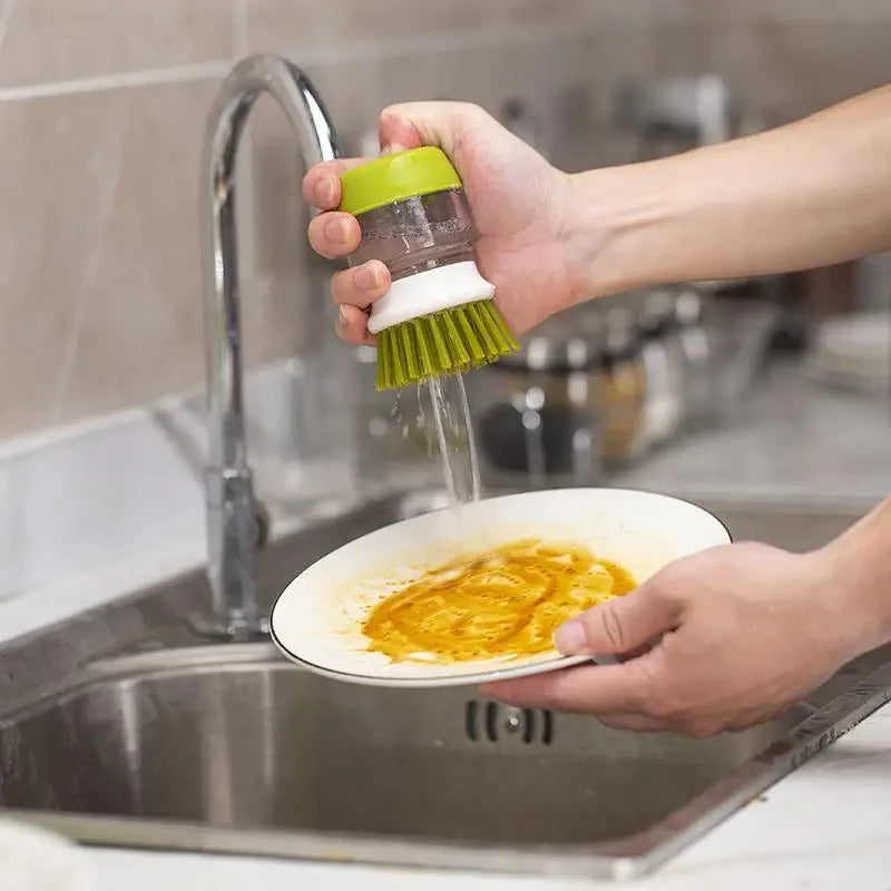 Person using a dish scrubber to clean a plate under running water in a kitchen sink.
